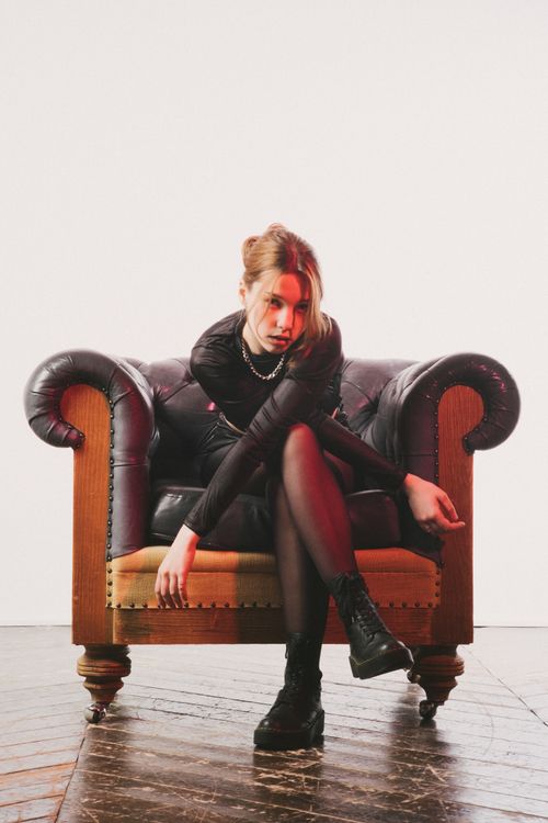 Free Stylish woman posing on a leather sofa chair in a studio setting. Stock Photo