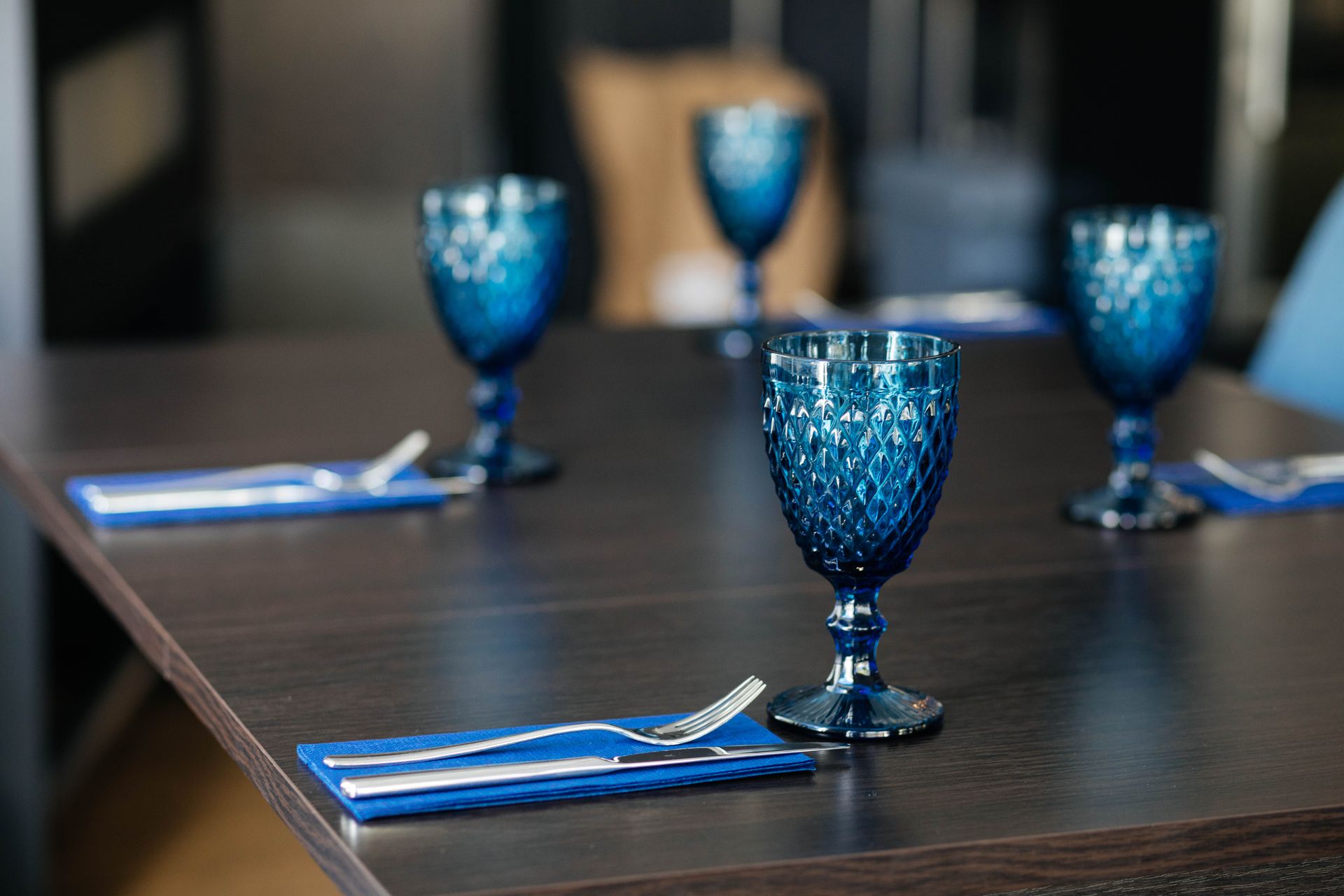 A beautifully set dining table featuring blue glassware and cutlery on a wooden surface.
