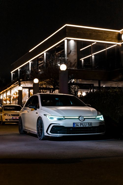 Free A Volkswagen Golf GTI parked on a city street at night, with illuminated lights and modern architecture. Stock Photo
