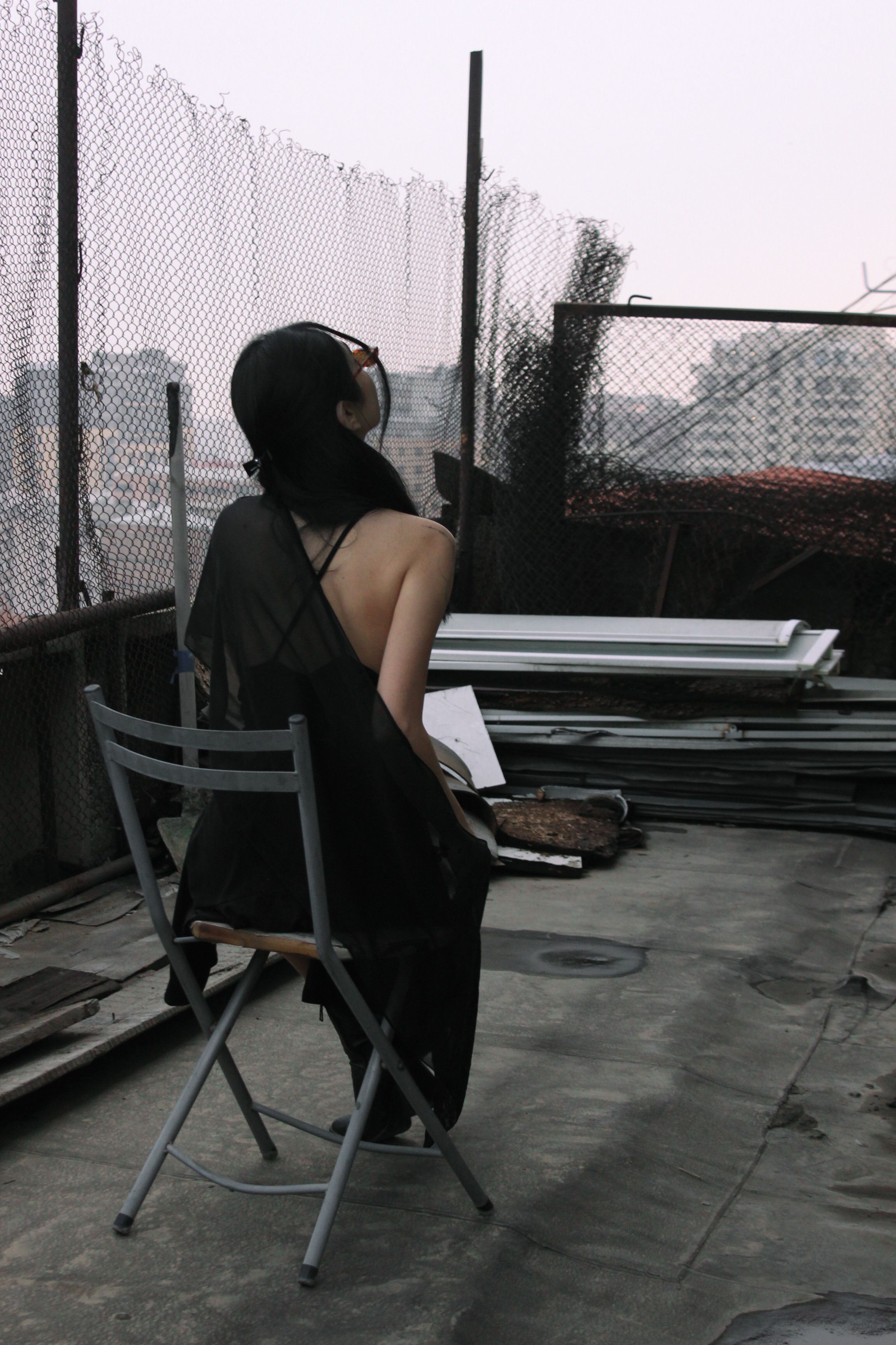 Woman in dark dress sitting on chair outdoors in industrial urban environment.