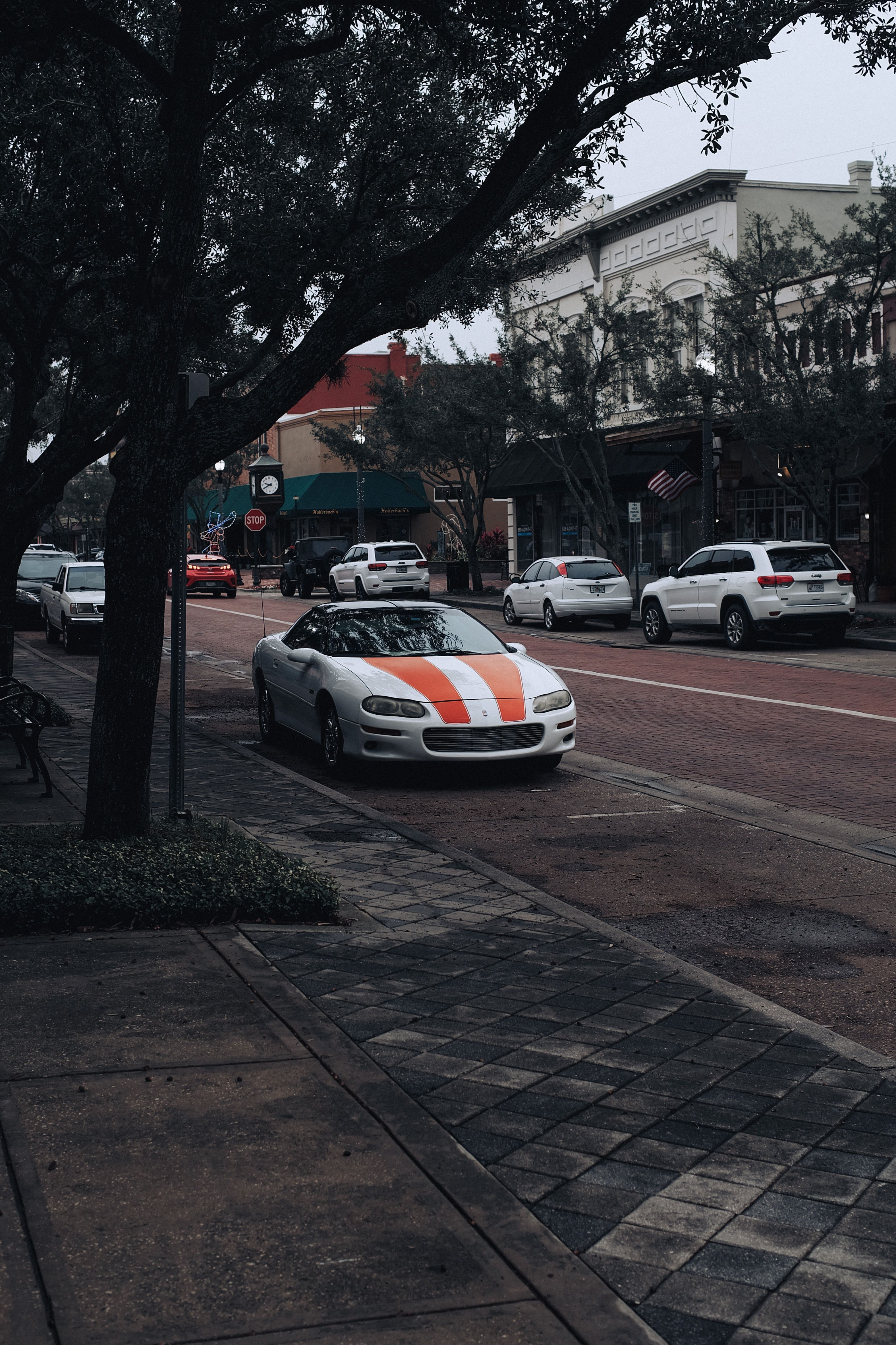 Fotomural Una vibrante vista urbana con coches aparcados, árboles y acera en un entorno urbano.