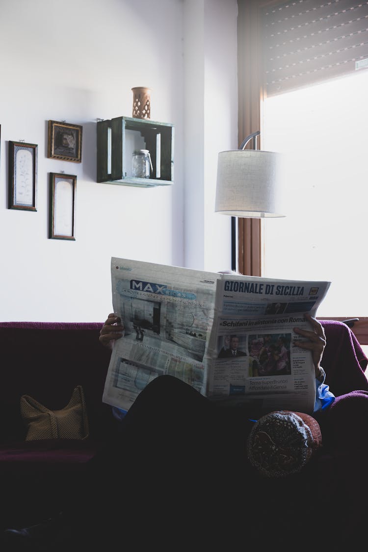 Person Sitting On Couch Reading Newspaper