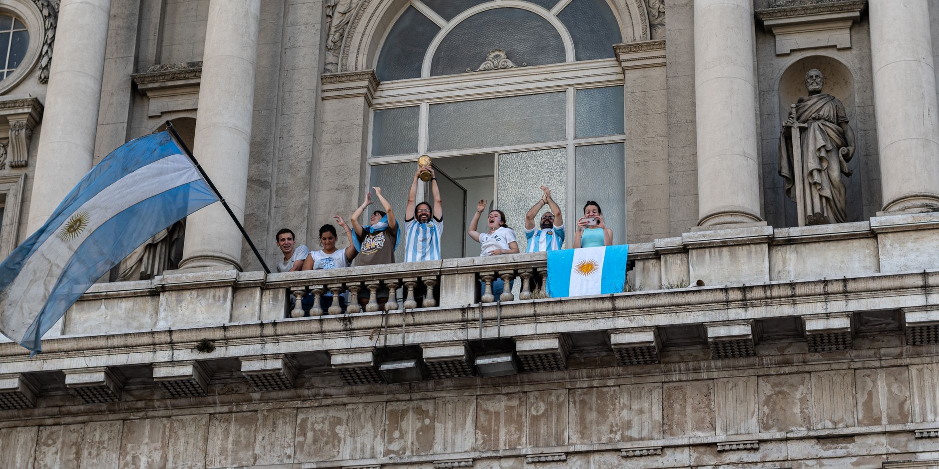 People celebrating with flags and a trophy on a Buenos Aires balcony.