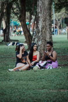 Three women sitting on grass in a park, chatting and laughing on a sunny day.