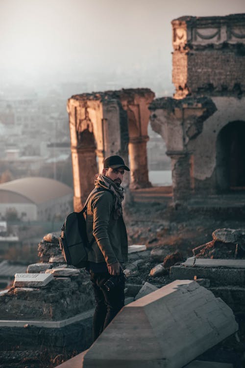 Man Wearing Cap and Backpack Standing on Ruins