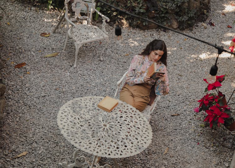 Woman Reading Books By Outdoor Table Set On Gravel