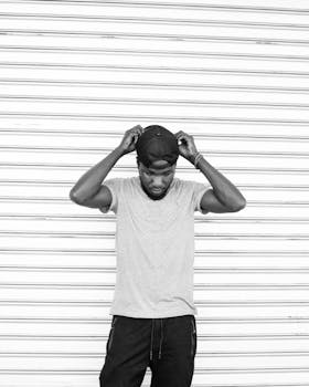 Striking black and white image of a man adjusting his cap, exuding style and confidence.