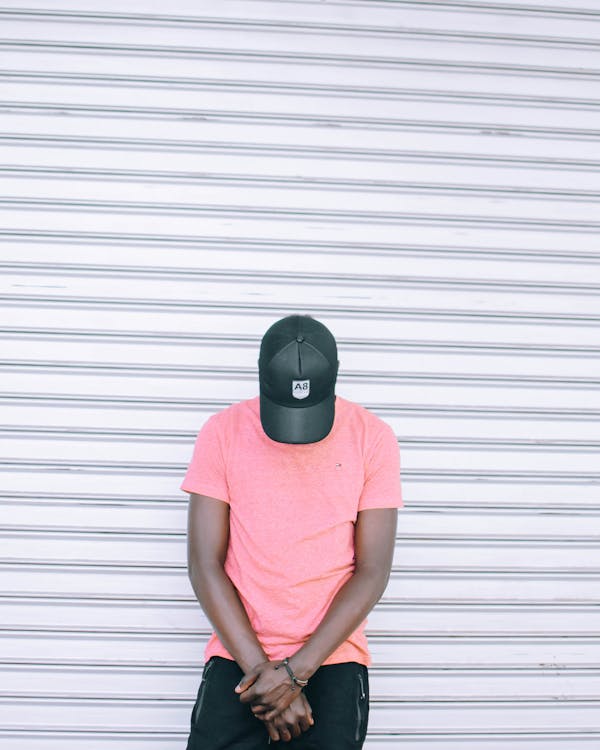 Man Wearing Pink Tee Shirt Leaning on Wall While Head Down