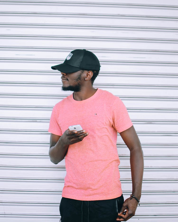 Man Wearing Pink T Shirt Holding Smartphone Standing Beside Grey Roll-up Door