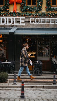 A man walking by a Christmas-decorated coffee shop on a cobblestone street.