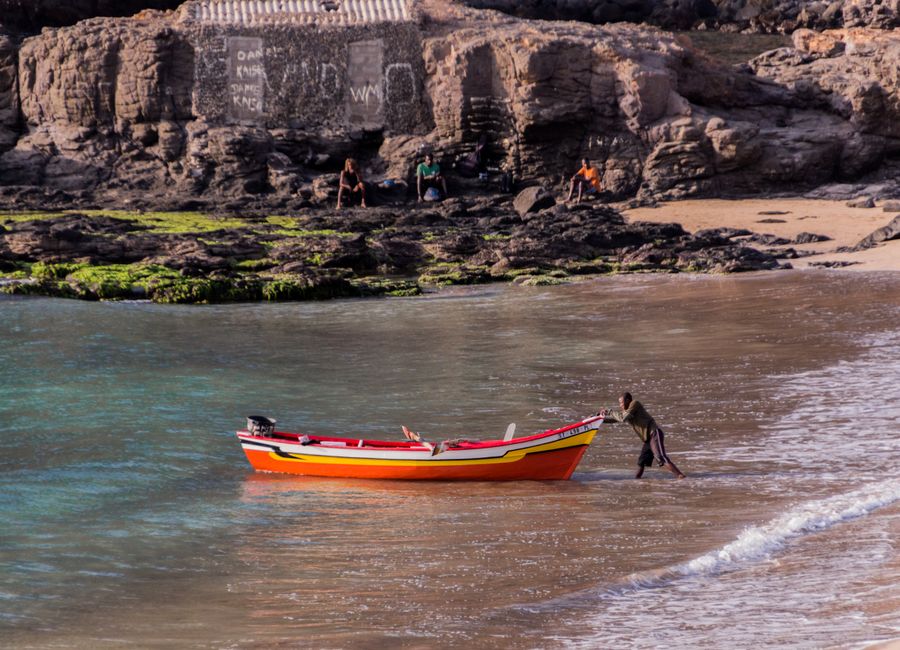 A fisherman pushes a colorful boat towards the shore of Tarrafal Beach in Cape Verde.