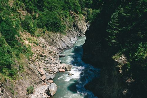 Free A scenic river flows through a lush, rocky gorge surrounded by dense greenery, capturing nature's beauty. Stock Photo