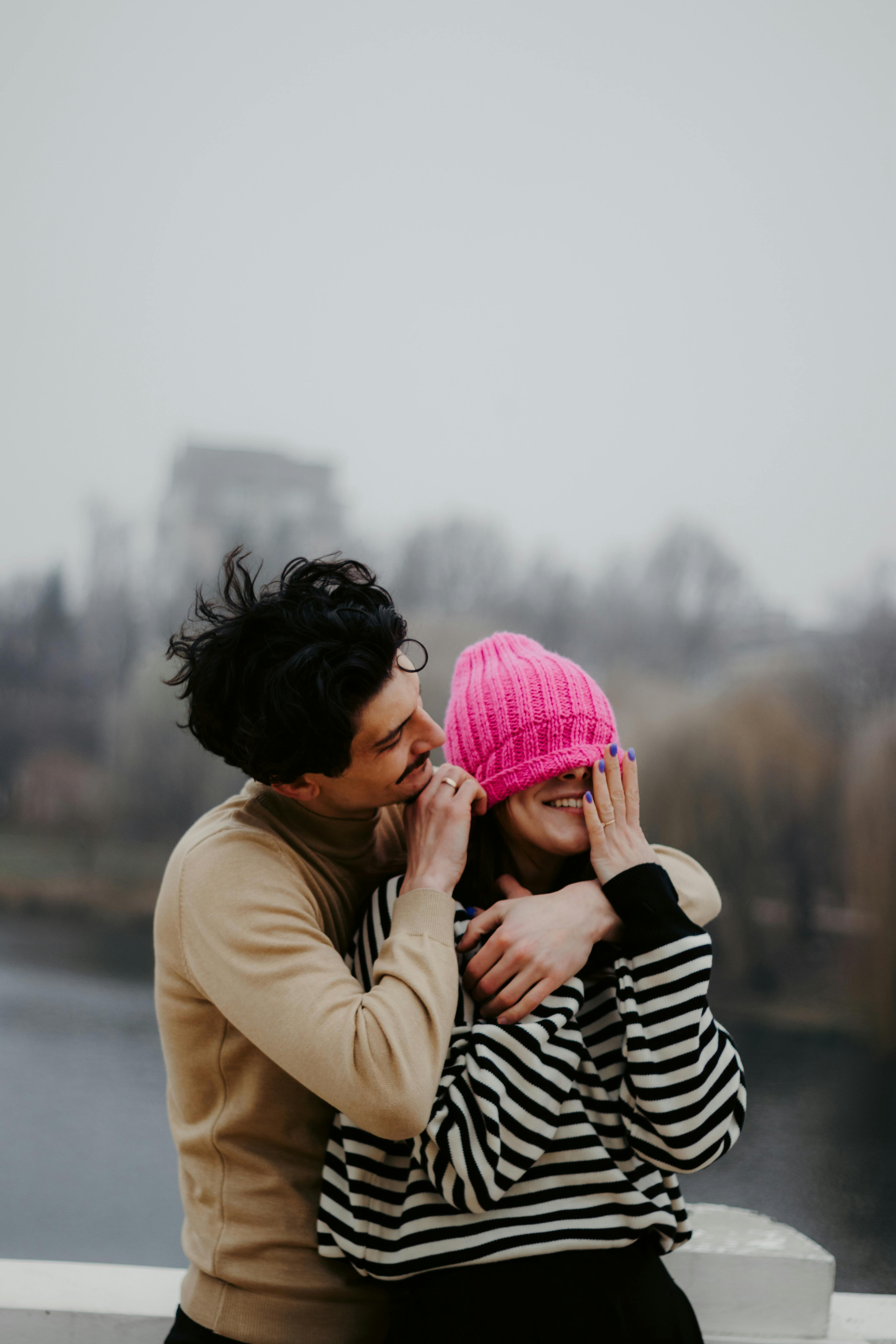 A couple shares a playful moment by the river in autumn with joy and laughter.