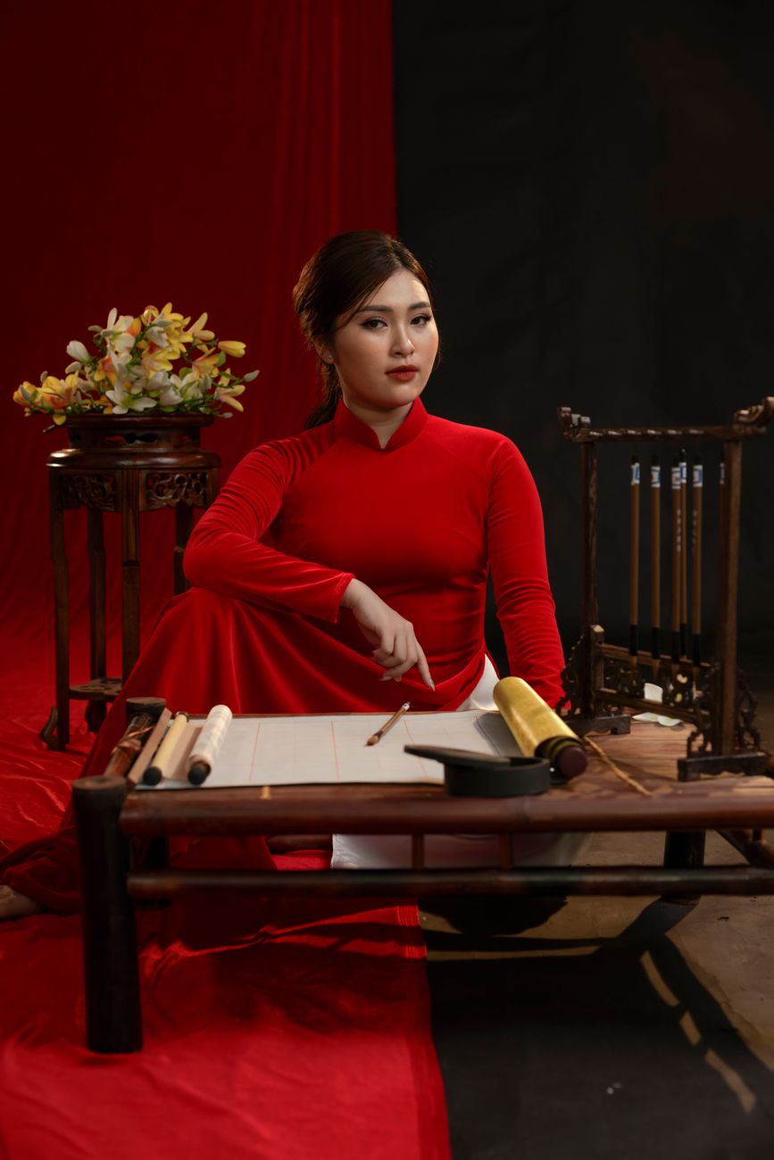 Portrait of an Asian woman wearing a red ao dai, seated elegantly indoors.