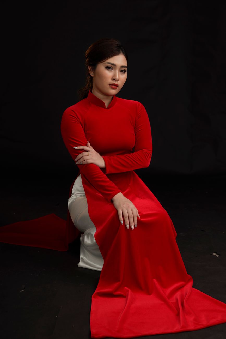 Elegant portrait of a woman in a red ao dai against a black studio background.