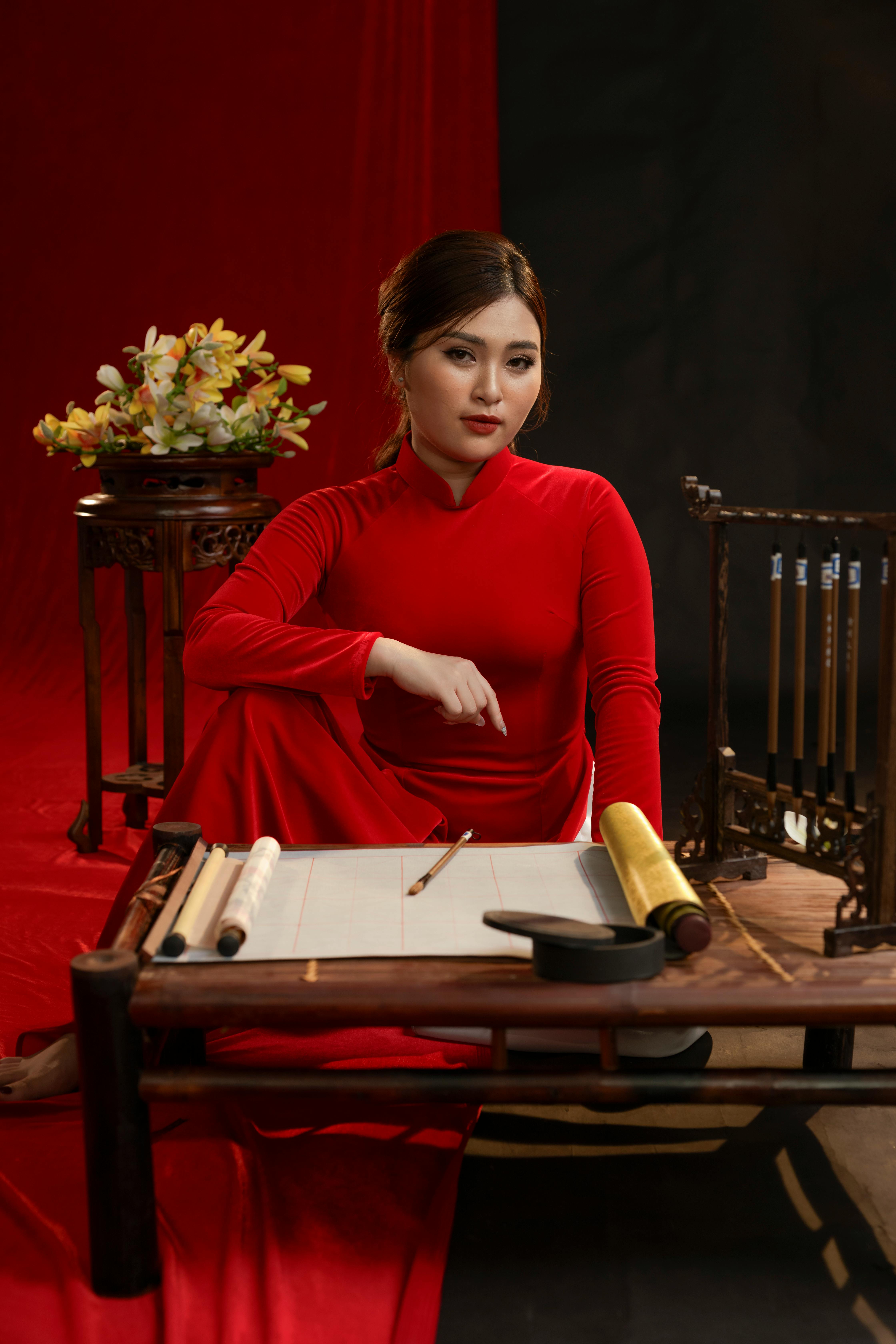 An elegant woman in a red Ao Dai seated with traditional accessories indoors.