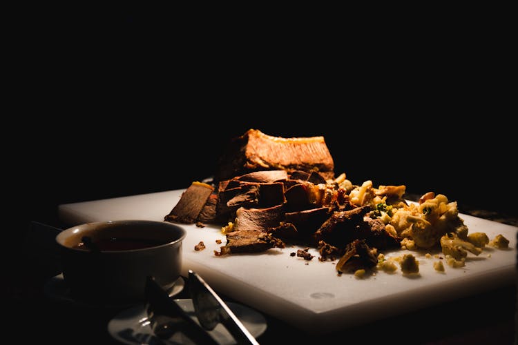 Roasted Meat And Broccoli Chunks On White Cutting Board In Darkness