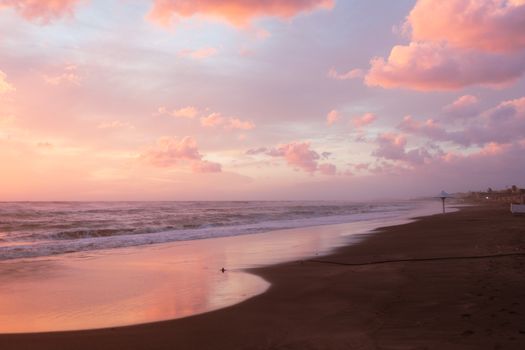 A tranquil beach scene at sunset with pink clouds reflecting on the sea.