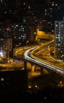 Dynamic cityscape featuring illuminated highways and light trails in a bustling urban environment during nighttime.