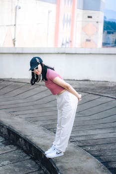 A stylish young woman in a cap and crop top poses on an urban rooftop in Cimahi, Indonesia.