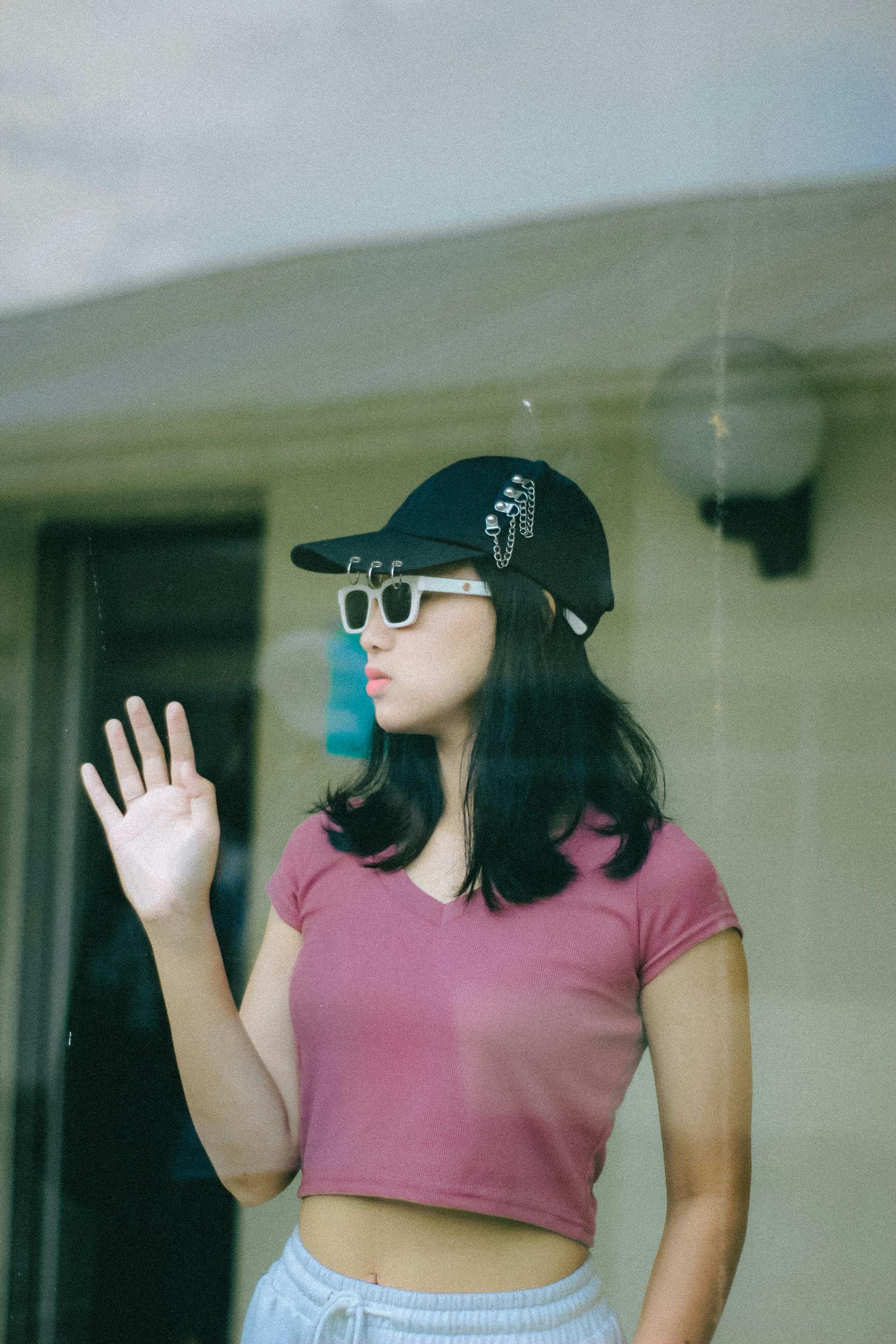 Young woman in casual attire and sunglasses waving indoors. Perfect for fashion and lifestyle themes.