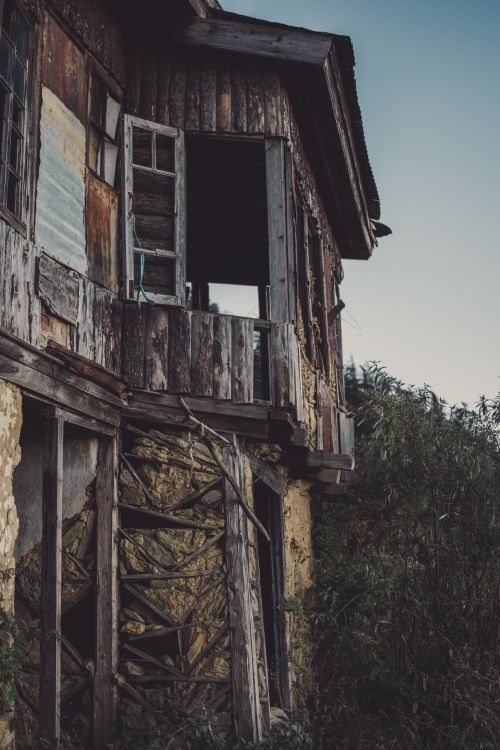 Free An old, abandoned wooden house with a rustic appearance, surrounded by overgrown vegetation. Stock Photo