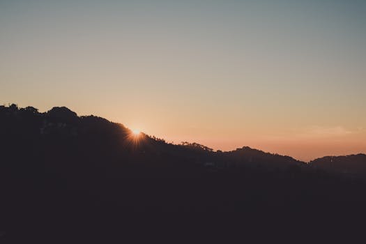 Beautiful sunset behind a mountain silhouette casting a warm glow over the landscape.