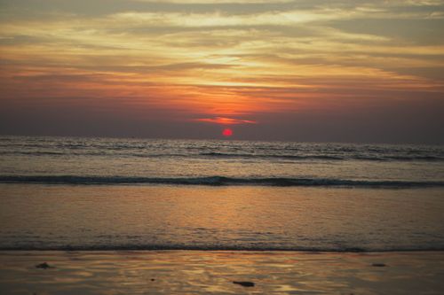 Free Calm beach at sunrise with vibrant colors reflecting on the serene sea, creating a peaceful atmosphere. Stock Photo