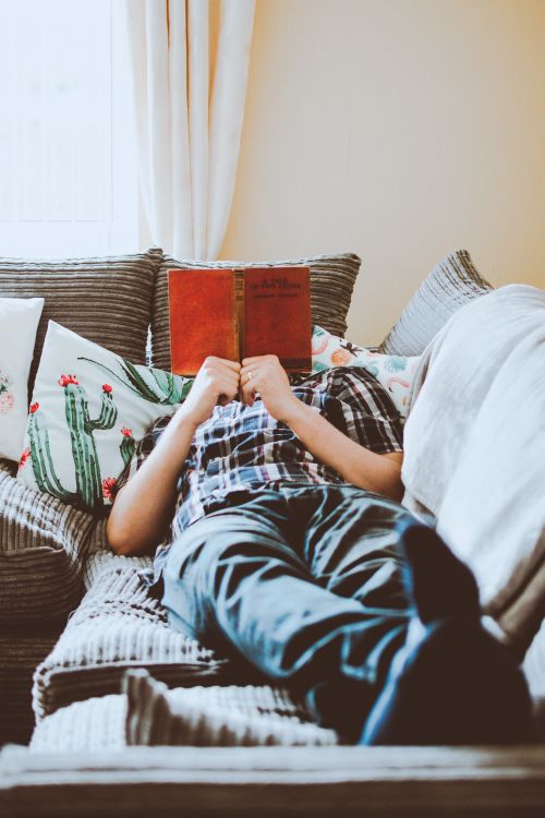 Free An adult lying on a sofa with a book, enjoying a relaxing moment indoors. Stock Photo