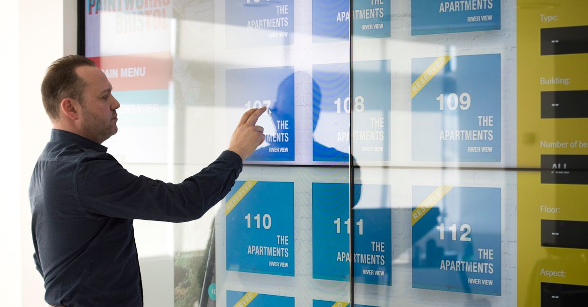A man in a black shirt looking at a digital screen showing apartments for rent in Bristol.