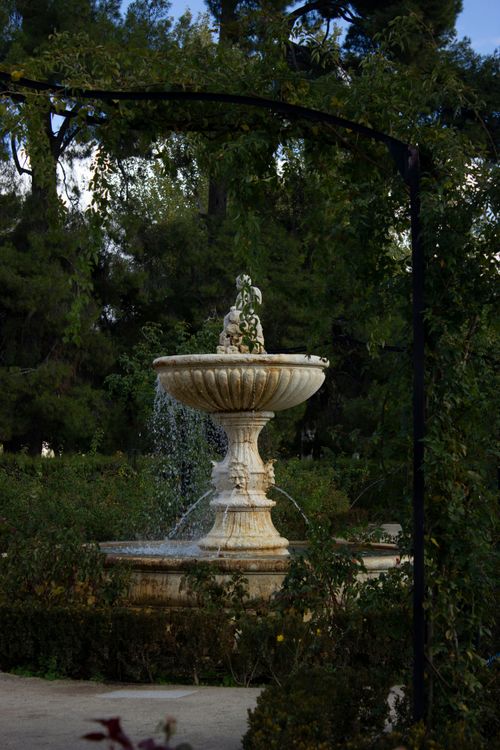Free Tranquil stone fountain surrounded by greenery in a lush garden. Stock Photo