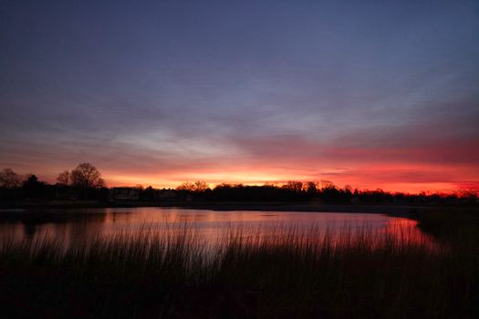 Beautiful sunset reflection over a calm lake surrounded by trees and grasses.