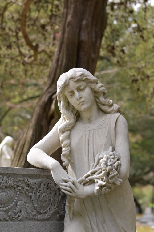 Free Elegant marble statue of a woman with flowers, set against a lush park backdrop, emanating serenity and classical beauty. Stock Photo