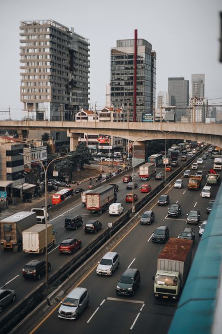 Traffic on a bustling Jakarta highway under urban skyscrapers and overpass.