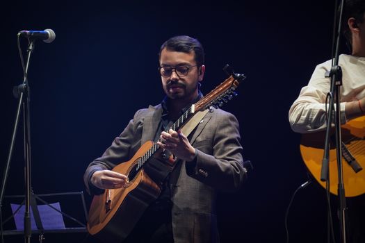 Musician playing acoustic guitar on stage with a microphone.