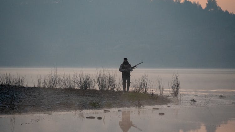 Man With A Rifle Waiting On Lakeshore