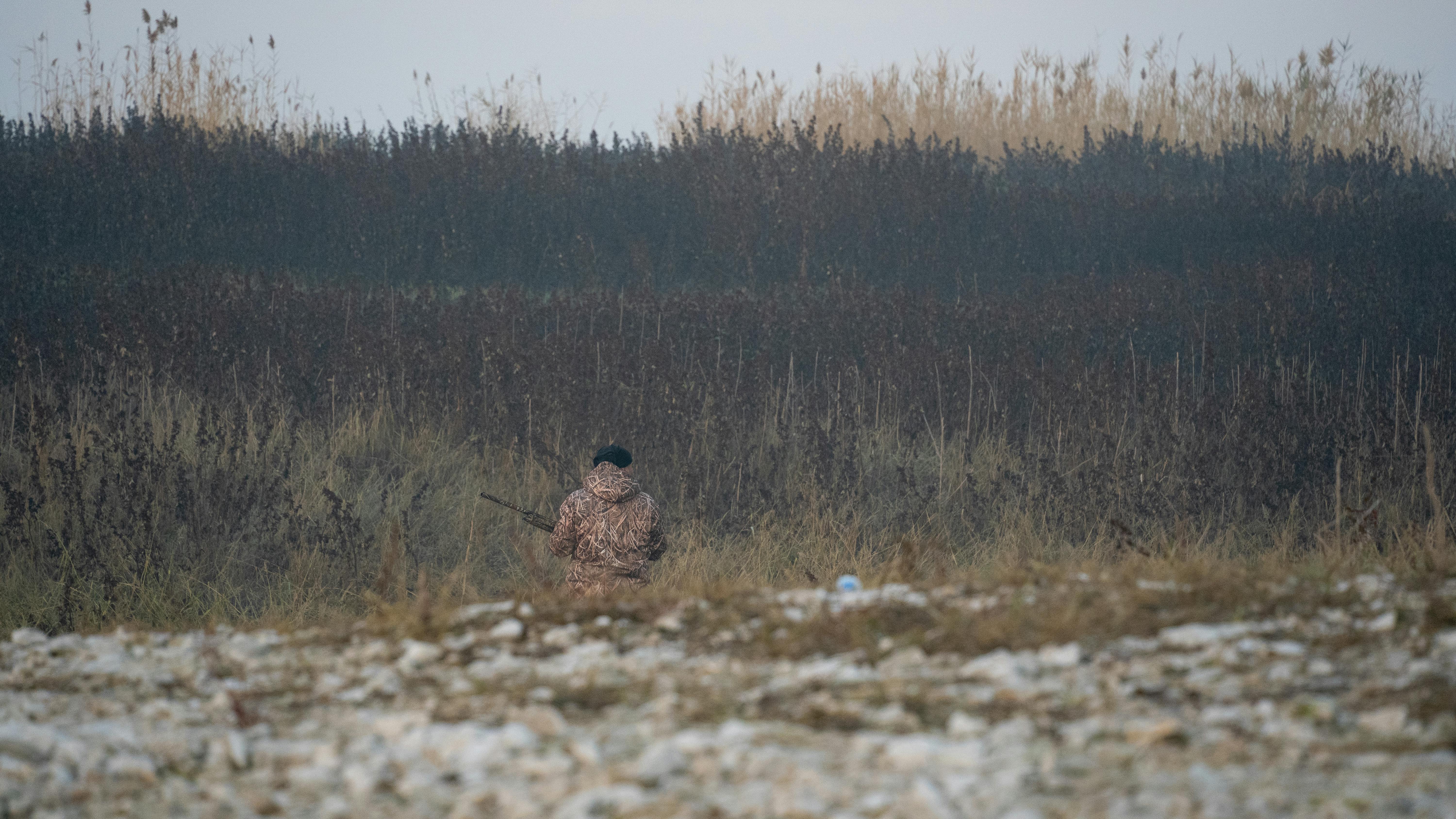 Back view of a hunter in camouflage in a rural winter setting.