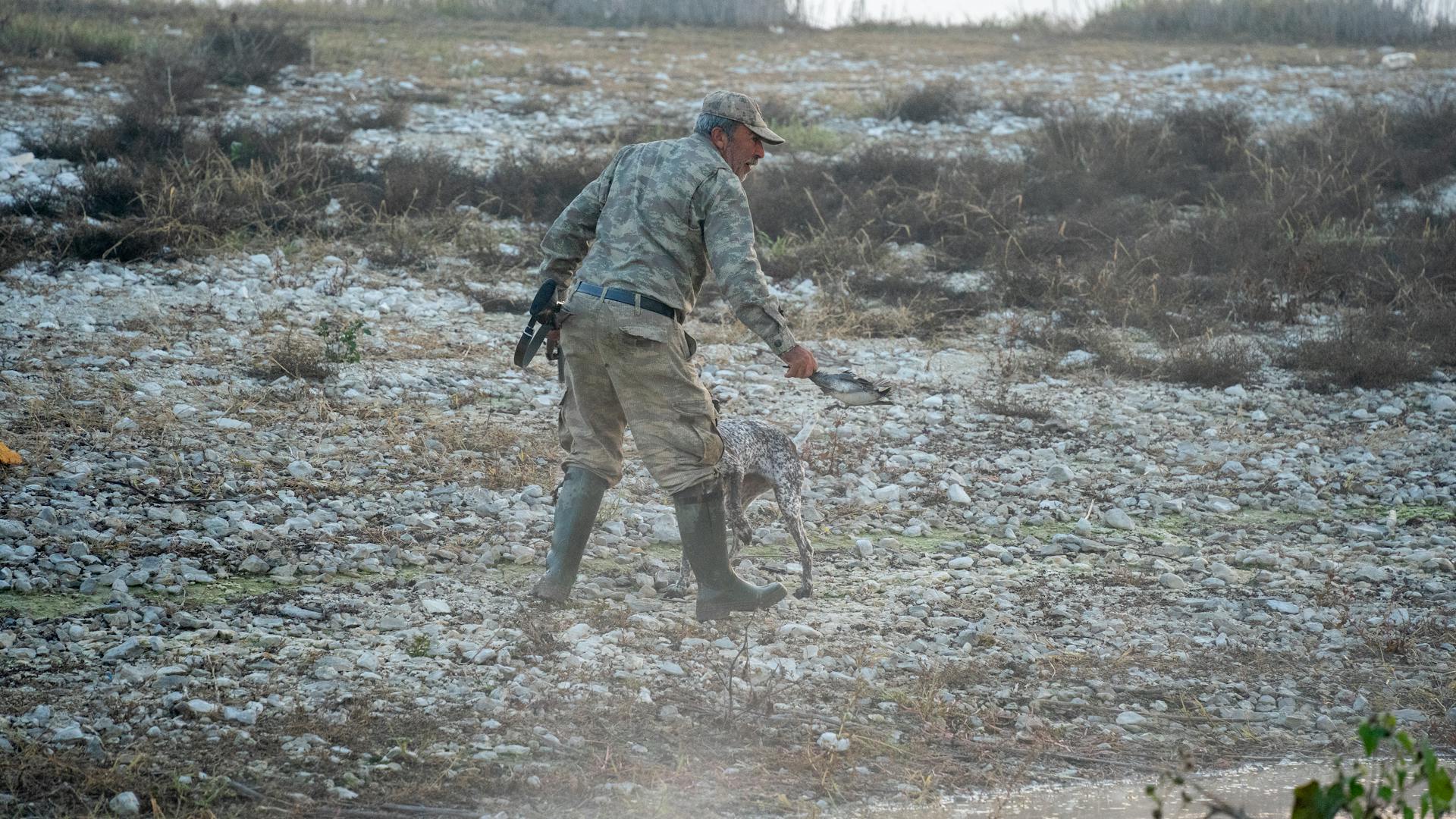 Man Wearing Camouflage Clothing Hunting in a Terrain with a Dog