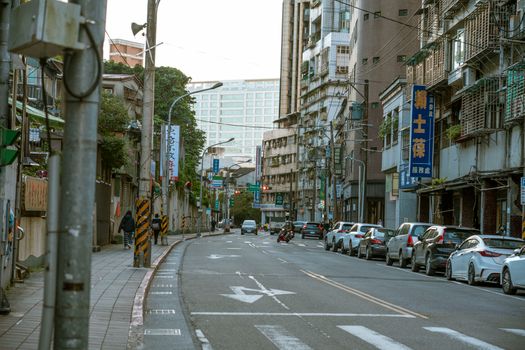 A busy urban street lined with parked cars and tall buildings in an Asian city.