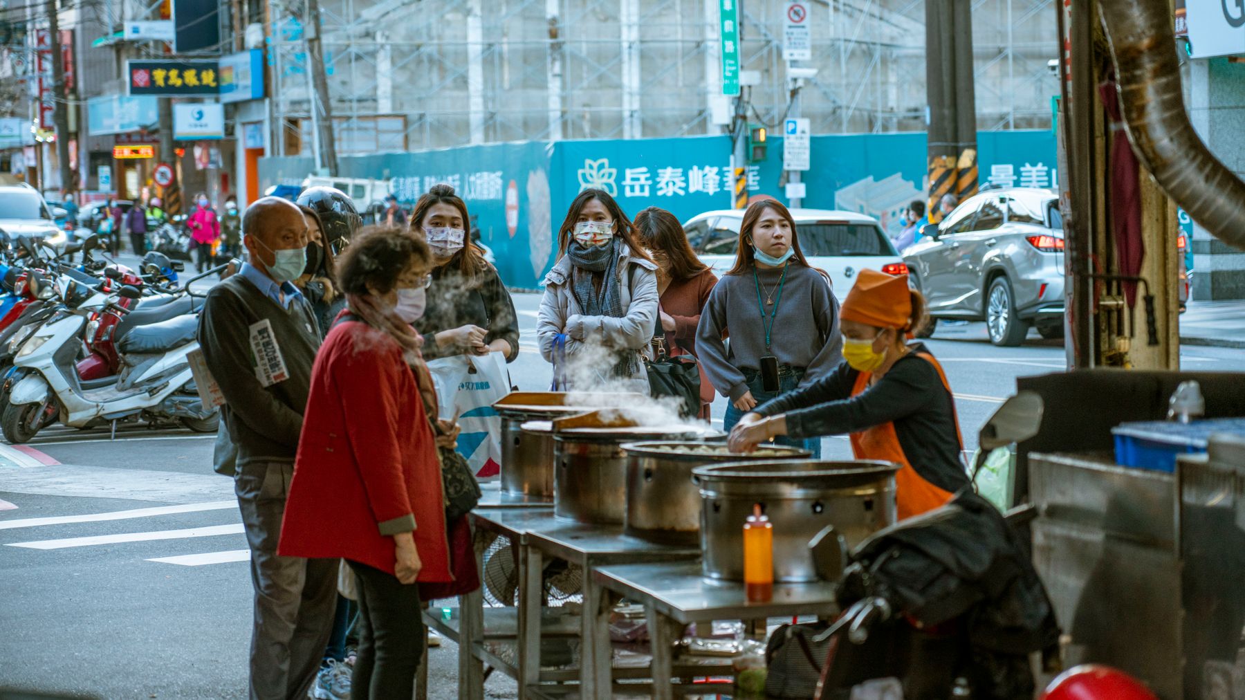 Des personnes portant des masques attendent de la nourriture de rue dans un cadre urbain, mettant en valeur la culture culinaire locale.