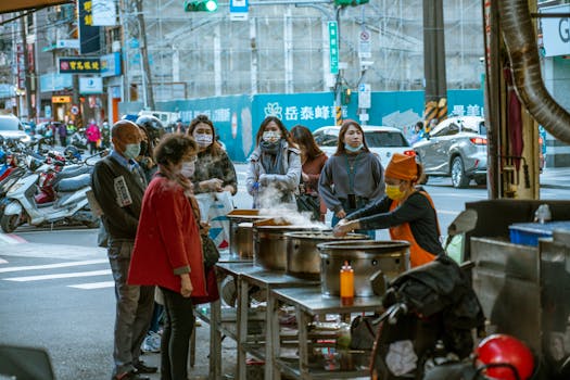 People wearing masks waiting for street food in an urban setting, highlighting local culinary culture.