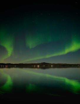 Captivating view of aurora borealis reflecting on a tranquil lake in Ölfus, Iceland under a starlit sky.