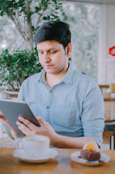 Adult man using a tablet in a relaxed cafe setting with coffee and dessert nearby.