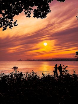 A couple walks along a seaside promenade during a vibrant sunset.