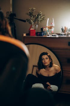 A woman gazes at her reflection in a round mirror, surrounded by home decor and soft lighting.
