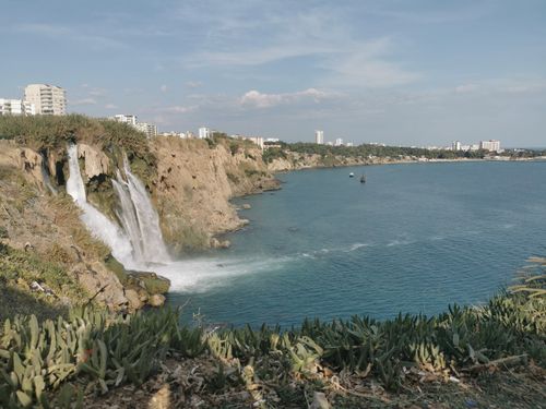 Free Picturesque view of a coastal waterfall with nearby cityscape, ideal for travel and nature themes. Stock Photo
