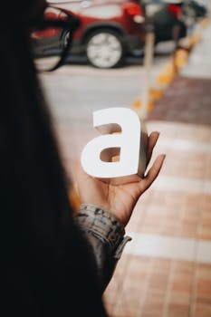 A person holds a 3D letter 'A' on a bustling street, Zapopan, Mexico.