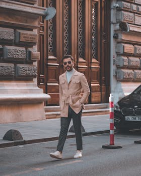 Stylish man in a beige jacket walking in an urban city setting, showcasing modern fashion.