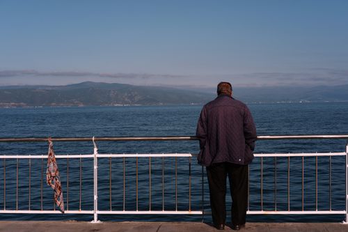 Free A man stands by the sea, gazing at the distant mountains, enjoying a serene moment of contemplation. Stock Photo