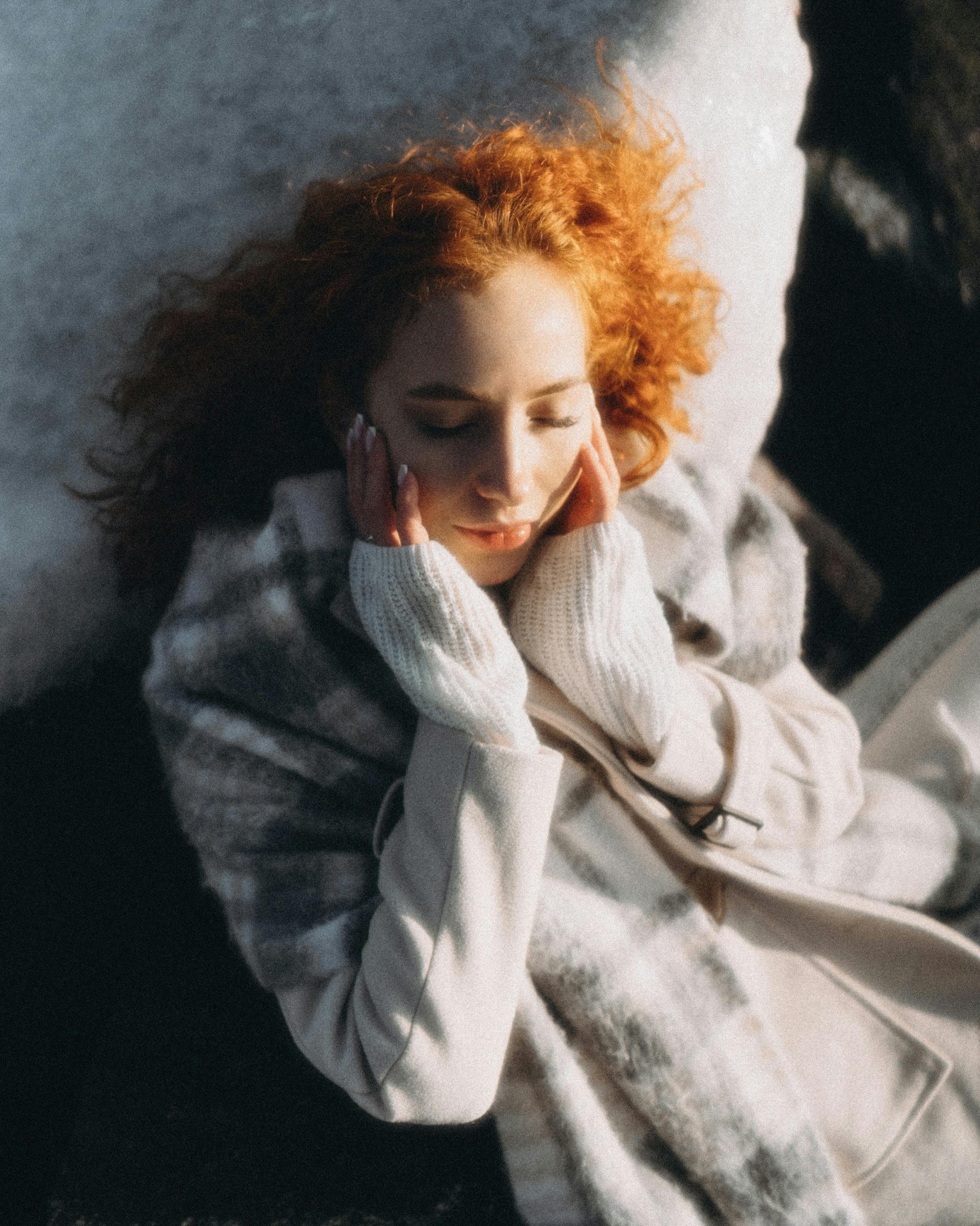 A peaceful redhead woman basking in the winter sun, wearing cozy clothing.